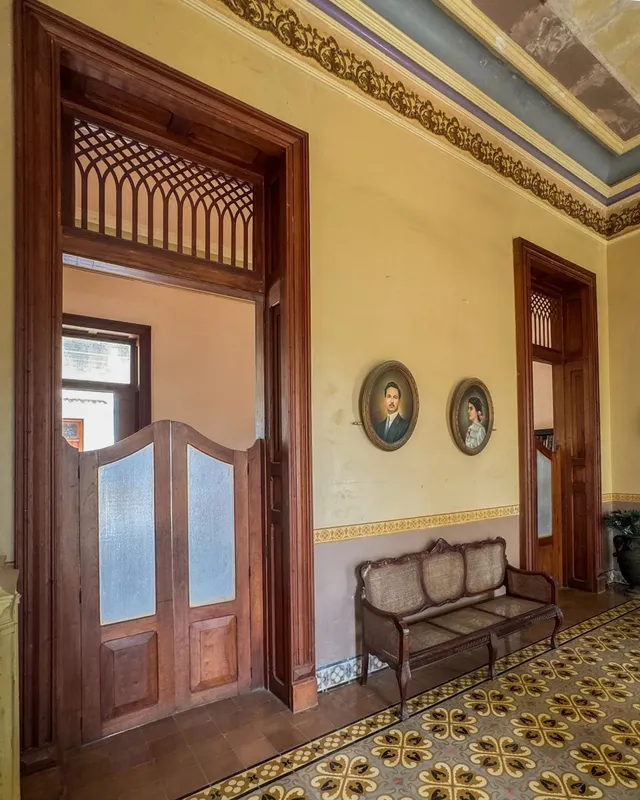 Corridor with two oval portraits, an antique bench and wooden doors with lattice transoms