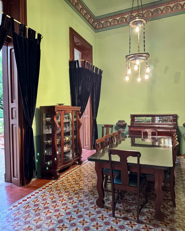 Dining room with green walls, a long wooden table, a display cabinet and a chandelier