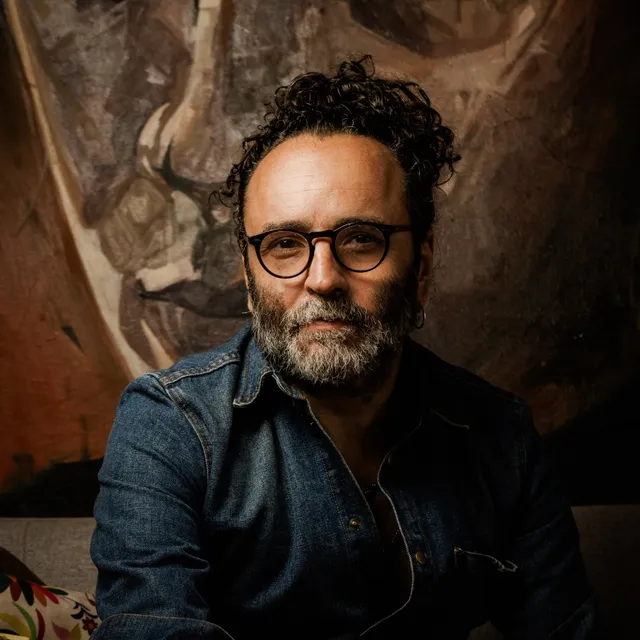 Portrait of Rodolfo Baeza in front of one of his paintings