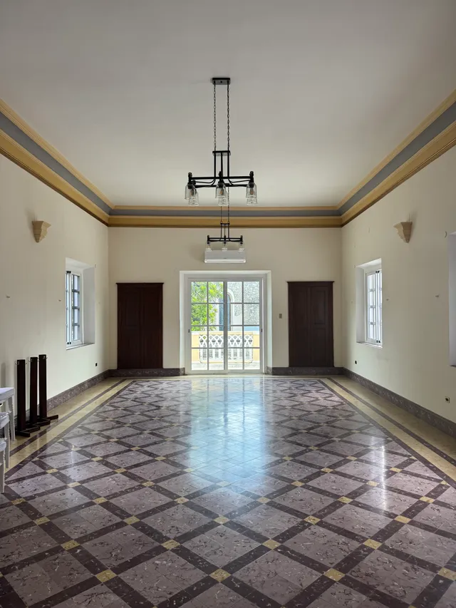 Large empty hall with a checkerboard marble floor, a central chandelier and doors to the balcony