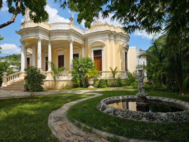 Yellow façade of Casona Cicero seen from the garden, with the fountain and its statue in the foreground