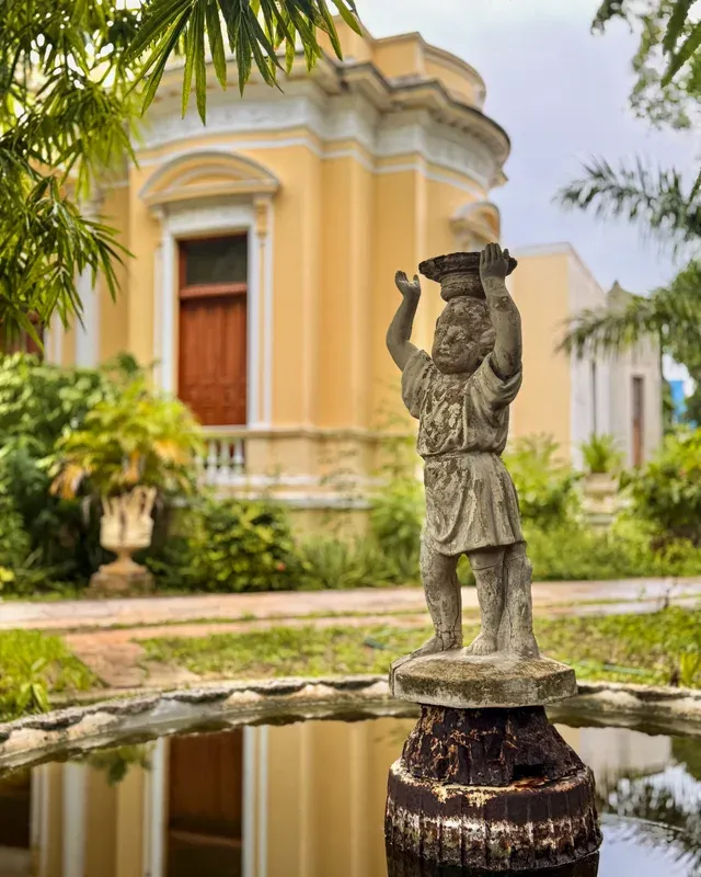 Statue of a child atop a fountain, with the yellow façade behind