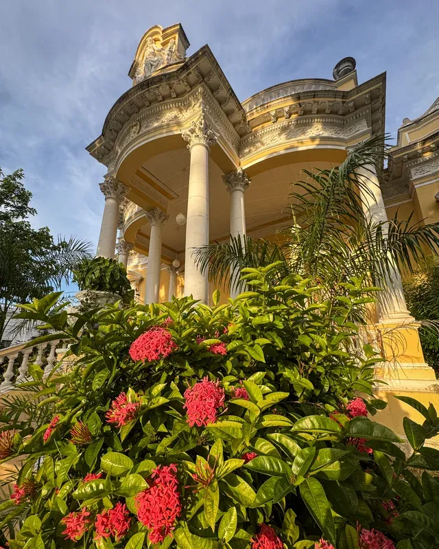 Corinthian-column portico with red flowers in the foreground and the yellow façade