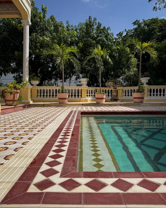 Red and green tiled pool beside the column corridor, surrounded by palm trees