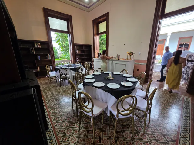 Biblioteca con mesas redondas de mantel negro y sillas doradas